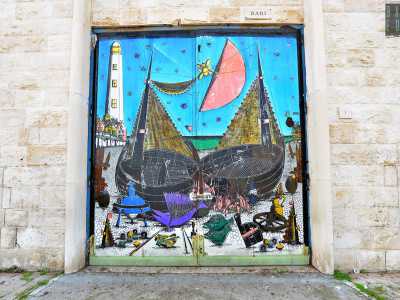 Porta Bari vanta la firma del pittore barese Gennaro Picinni, scomparso nel 2022. Su di essa sono raffigurate due imponenti barche pronte a salpare, con il Faro di San Cataldo sullo sfondo e il cielo azzurro dominato da una grande luna rossa (foto di Nicola Velluso)